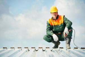 A commercial roofing contractor crouching on top of a metal roof.