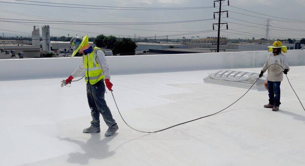 Two men are spraying a white roof with a hose.